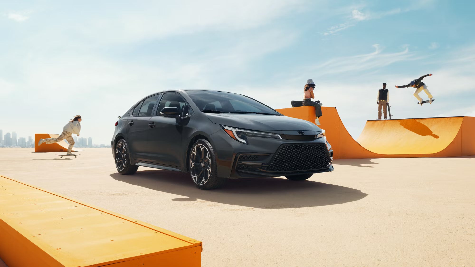 A gray car sitting parked at a skate park.