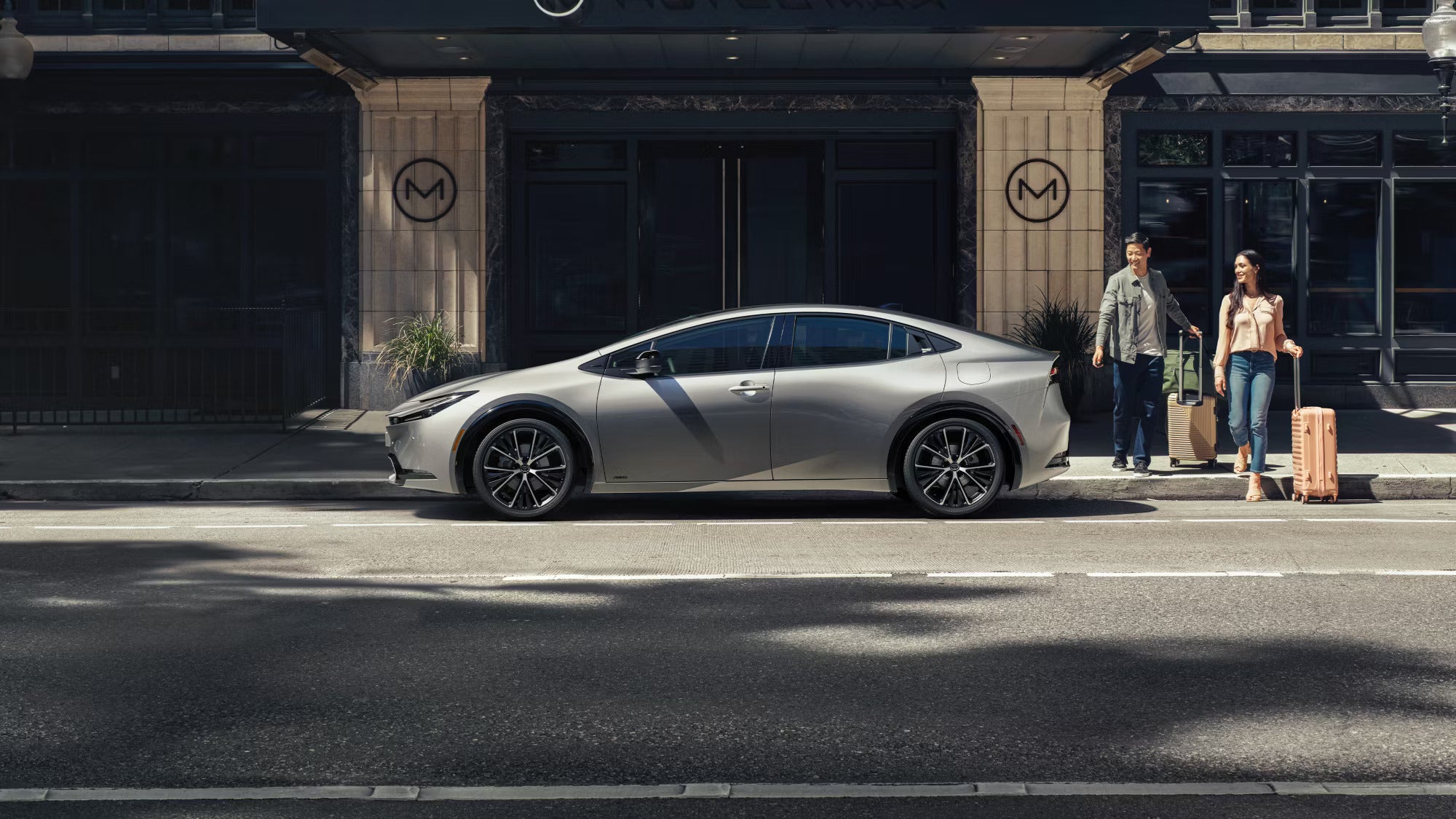 Two people walking next to a silver car.