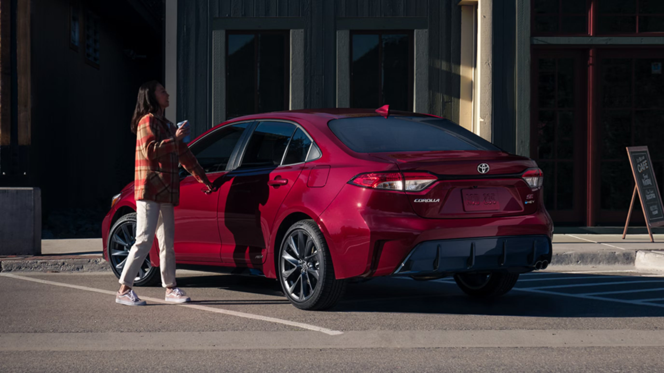 A girl walking to a red car parked.