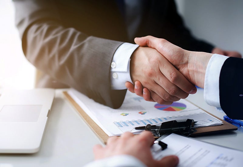 two people shaking hands with financial documents on a clipboard between them